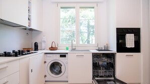 Une cuisine moderne équipée d’un lave-linge et d’un sèche-linge intégrés, d’un évier et d’une fenêtre donnant sur les arbres.