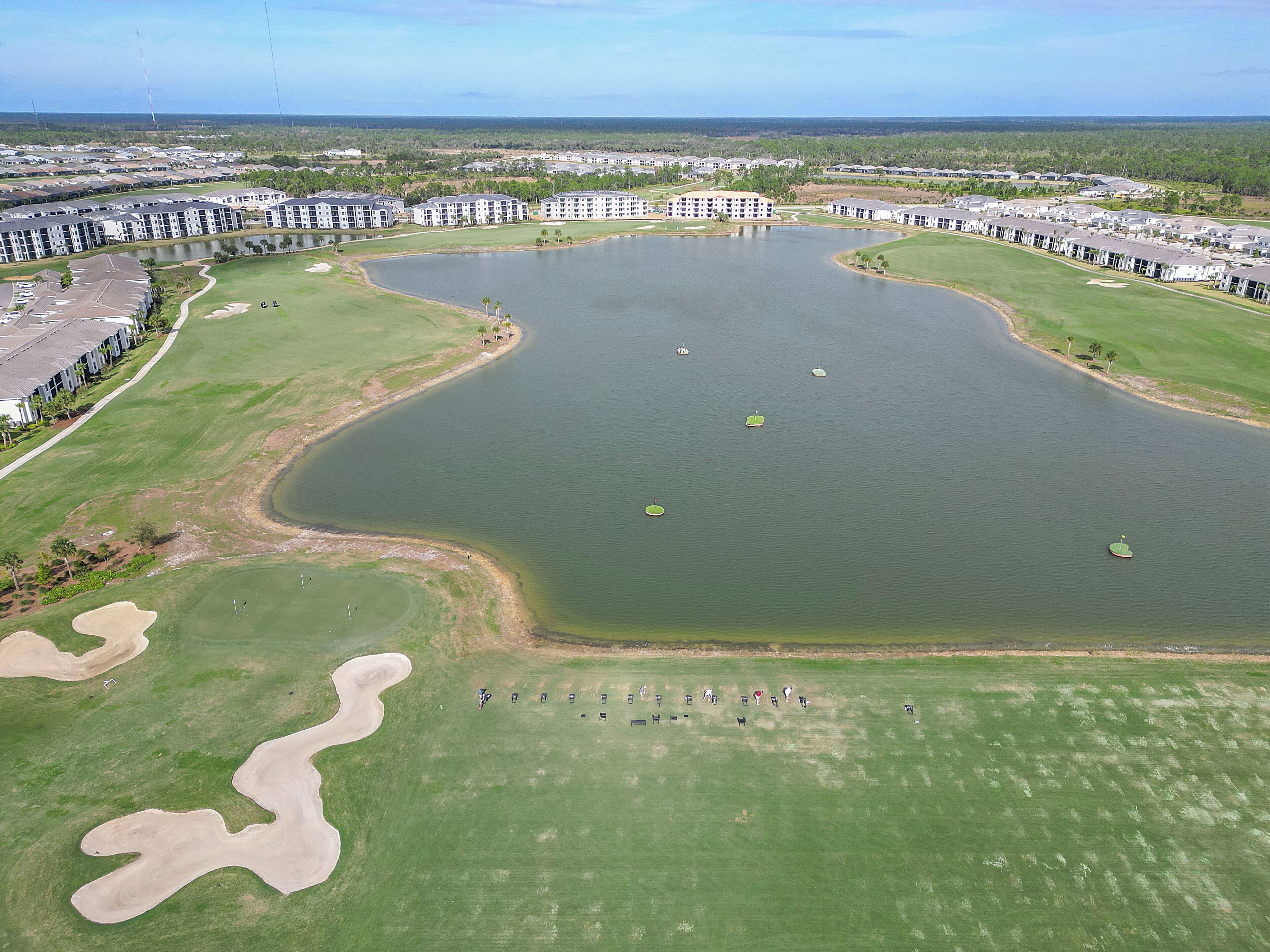 An aerial view of a golf course with a large pond, surrounded by buildings and greenery.
