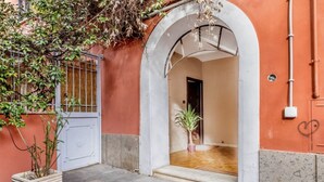 An arched entrance to a building with a tiled floor, a potted plant, and a metal gate. - Deco Garden Apartment Trastevere (Roma)