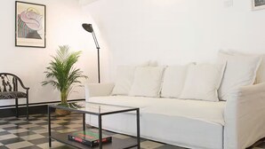 A living room with a white sofa, a glass coffee table, a black floor lamp, a potted plant, and a framed picture on the wall. - Deco Garden Apartment Trastevere (Roma)