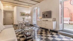 A living room with a checkered floor, a sofa, a coffee table, a TV, a dining area with chairs, and a white cabinet. - Deco Garden Apartment Trastevere (Roma)