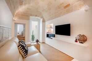 A modern living room with a stone ceiling, a white sofa, a flat-screen TV, and a decorative vase. - Infinito Luxury Suite by BarbarHouse (Monopoli)