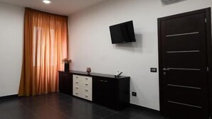 A room with a dark tiled floor, a black cabinet with drawers, a flat-screen TV mounted on the wall, and a dark door. - Sofia e la città delle meraviglie (Naples)