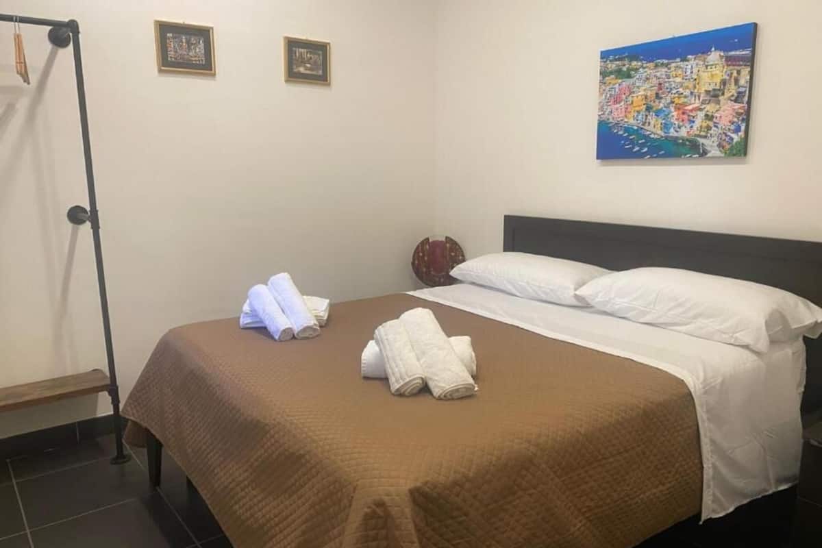 Une chambre d’hôtel avec un lit, des serviettes blanches, une couverture marron et un tableau représentant une ville côtière accroché au mur.