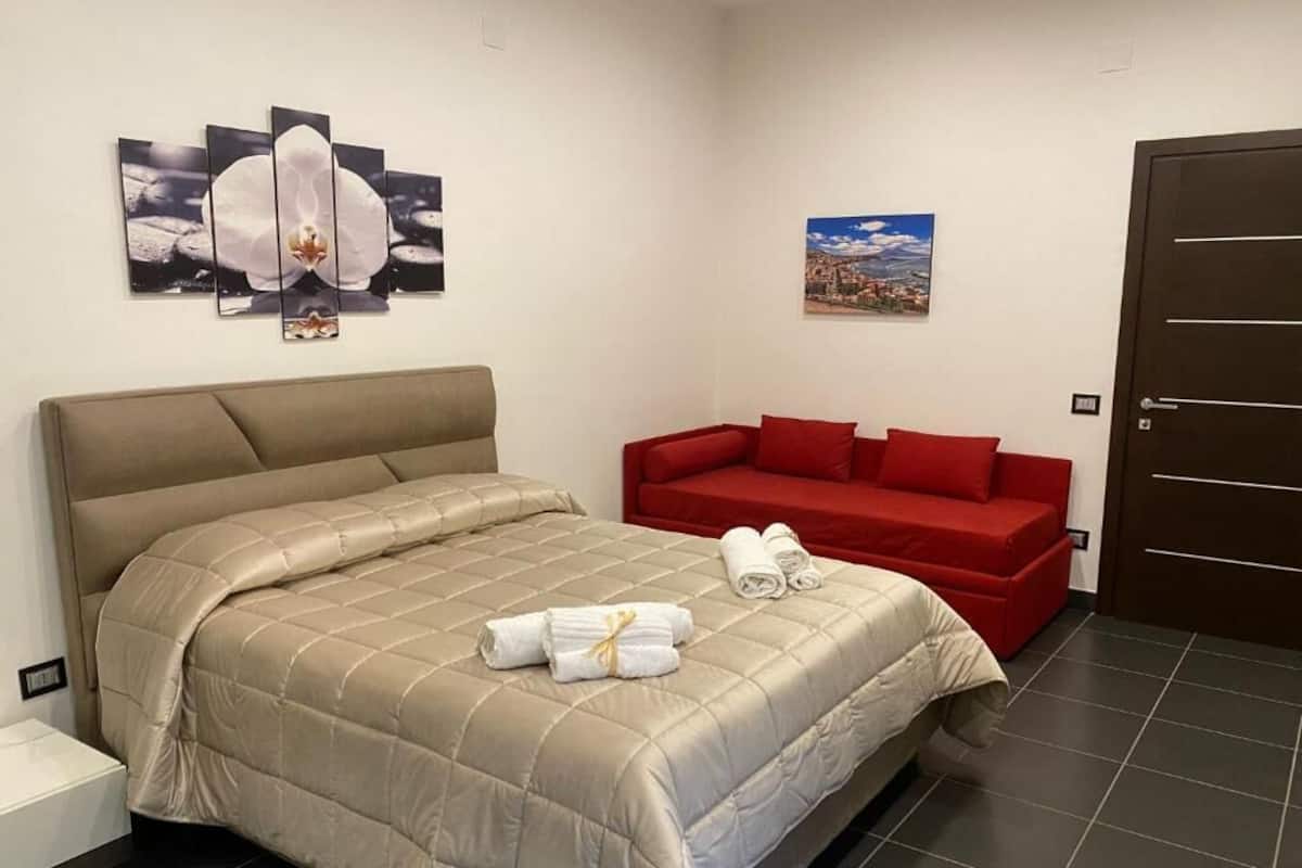Une chambre d’hôtel avec un lit, un canapé rouge et des œuvres d’art accrochées aux murs.