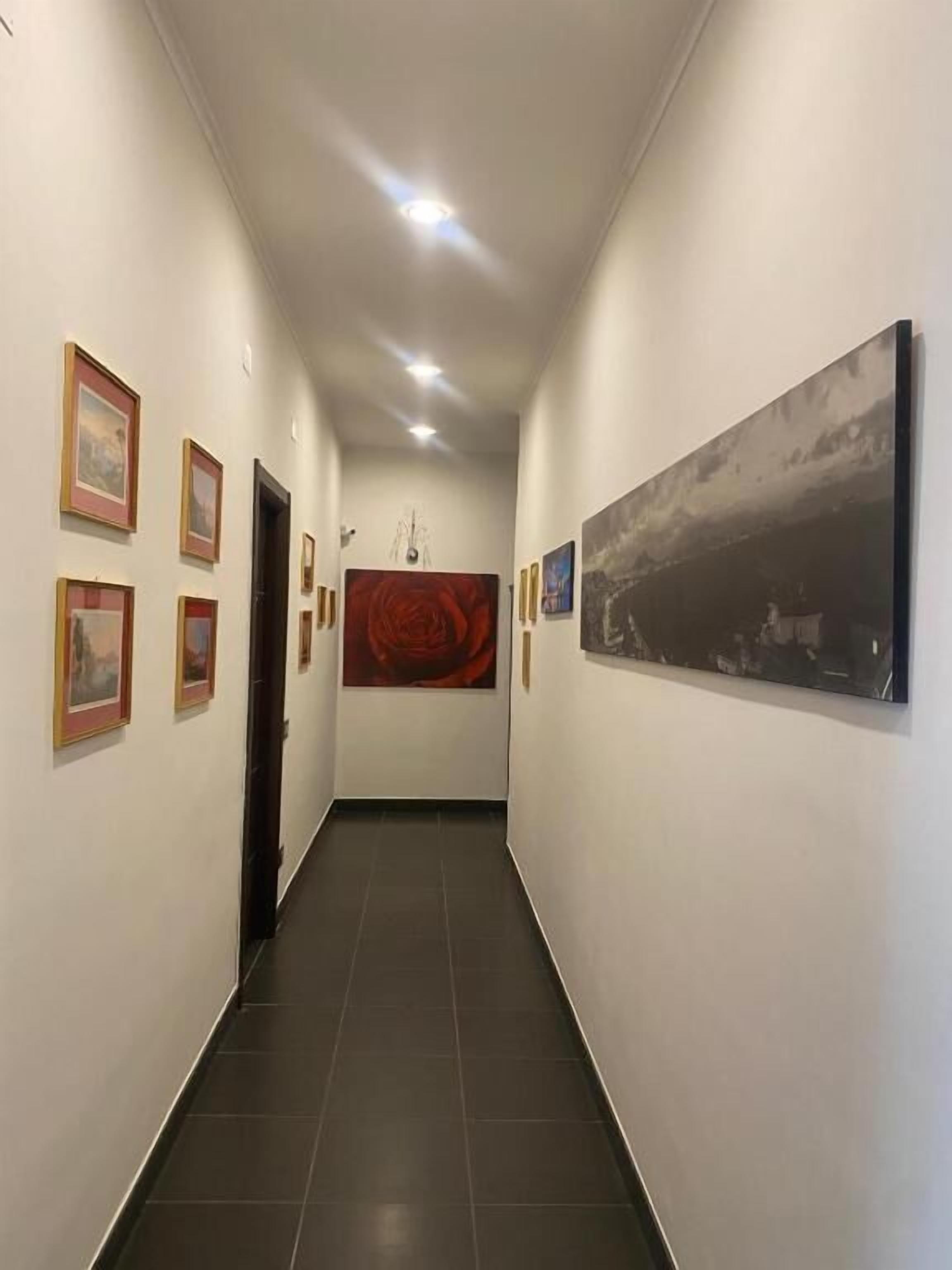 Un pasillo con obras enmarcadas en las paredes, un cuadro abstracto de gran tamaño y una puerta al final.