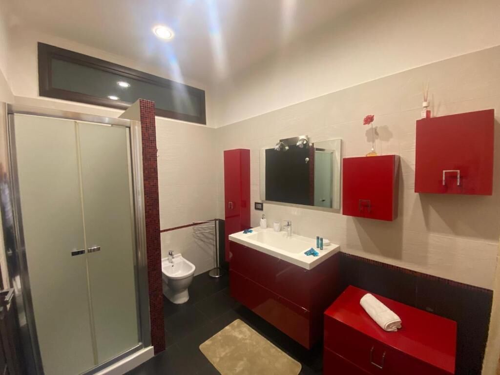 A modern bathroom with a glass shower enclosure, a white sink with a red vanity, and a red towel on the counter.