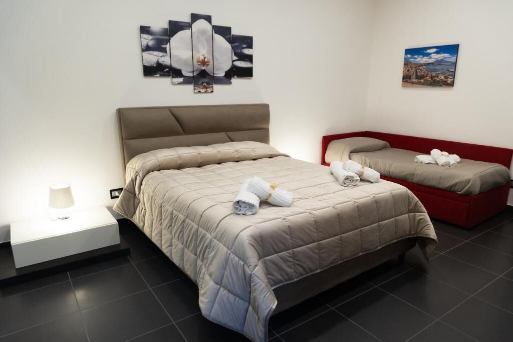 A hotel room with a large bed, a smaller bed, a nightstand with a lamp, and artwork on the walls.
