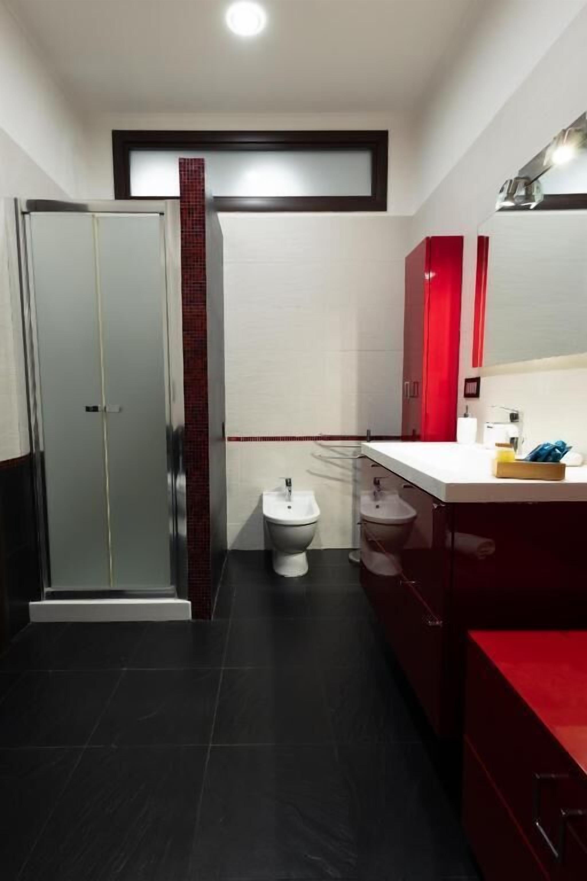 A modern bathroom with a glass shower enclosure, a white toilet, and a red vanity with a mirror.