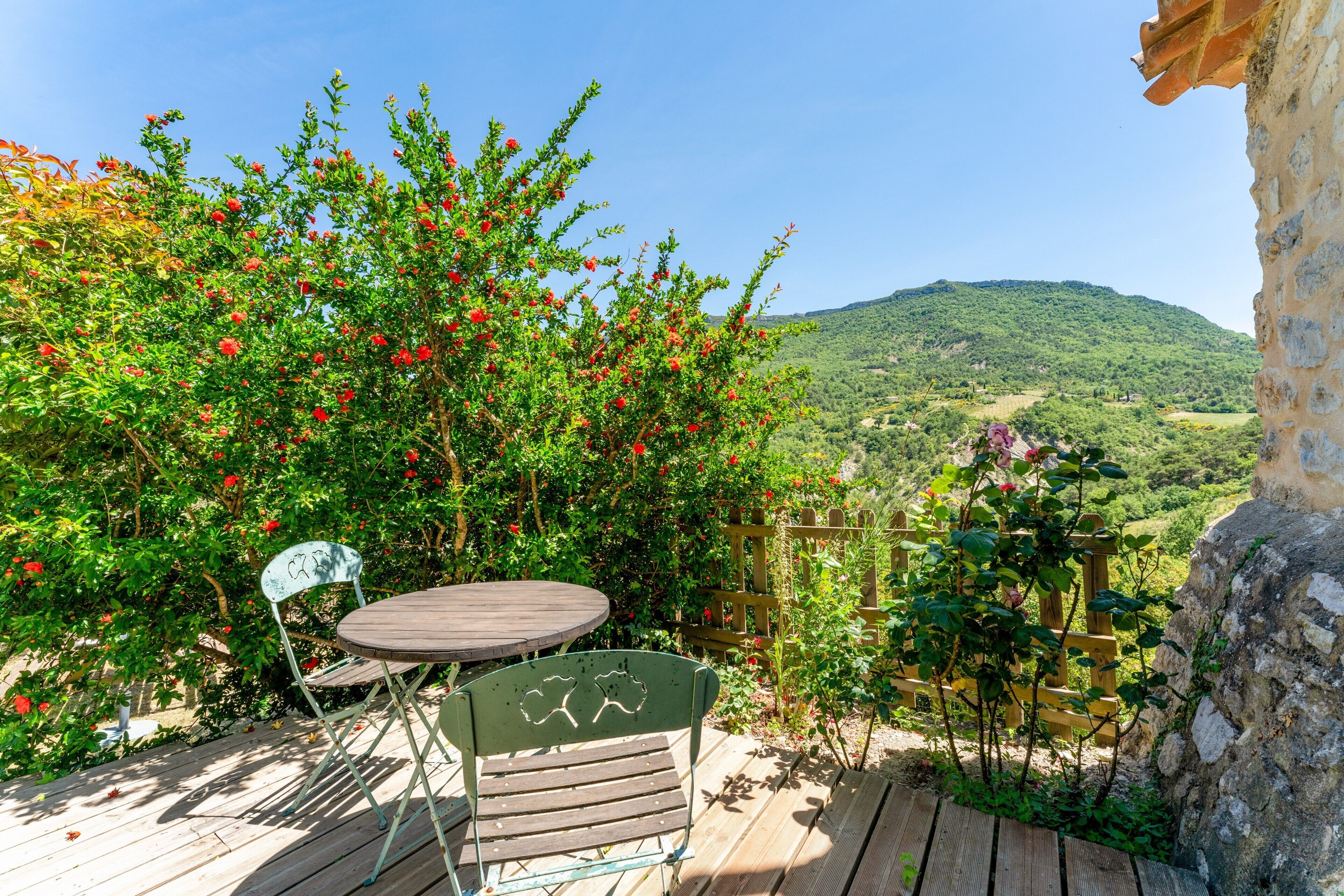 Une terrasse en bois avec une table et des chaises, entourée d’une végétation luxuriante et offrant une vue sur un paysage vallonné.