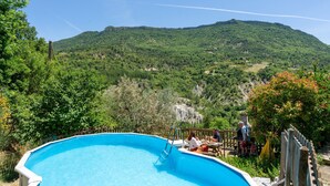 A swimming pool with a wooden deck and a view of a mountainous landscape. - Le frêne – La Ferme des Aygues, Drôme Provençale (Montaulieu)