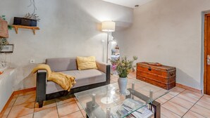 A living room with a sofa, a glass coffee table, a lamp, a vase with flowers, and a wooden chest. - Le frêne – La Ferme des Aygues, Drôme Provençale (Montaulieu)