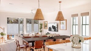 Un vaste espace dédié à la salle à manger, avec une grande table en bois, des chaises en osier et des lampes en osier suspendues au plafond.