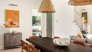 Un coin repas avec une table en bois foncé, des suspensions en rotin et un buffet orné d’un vase.