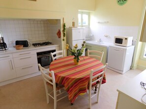 A kitchen with white cabinets, a stove, oven, microwave, and a dining table with chairs.