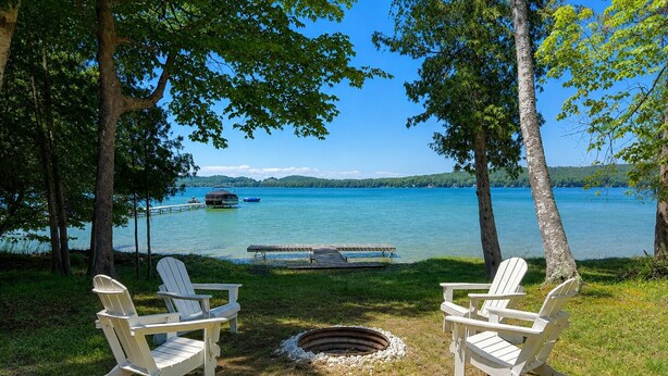 Zwei Adirondack-Stühle mit Blick auf einen See, auf dem Boote fahren, mit einem Steg und einer Rasenfläche mit Feuerstelle.