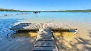 Eine Holzsteganlage, die sich in einen ruhigen See mit klarem Wasser erstreckt, umgeben von Hügeln.