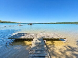 Un muelle de madera se extiende sobre un lago tranquilo con agua cristalina, rodeado de colinas.