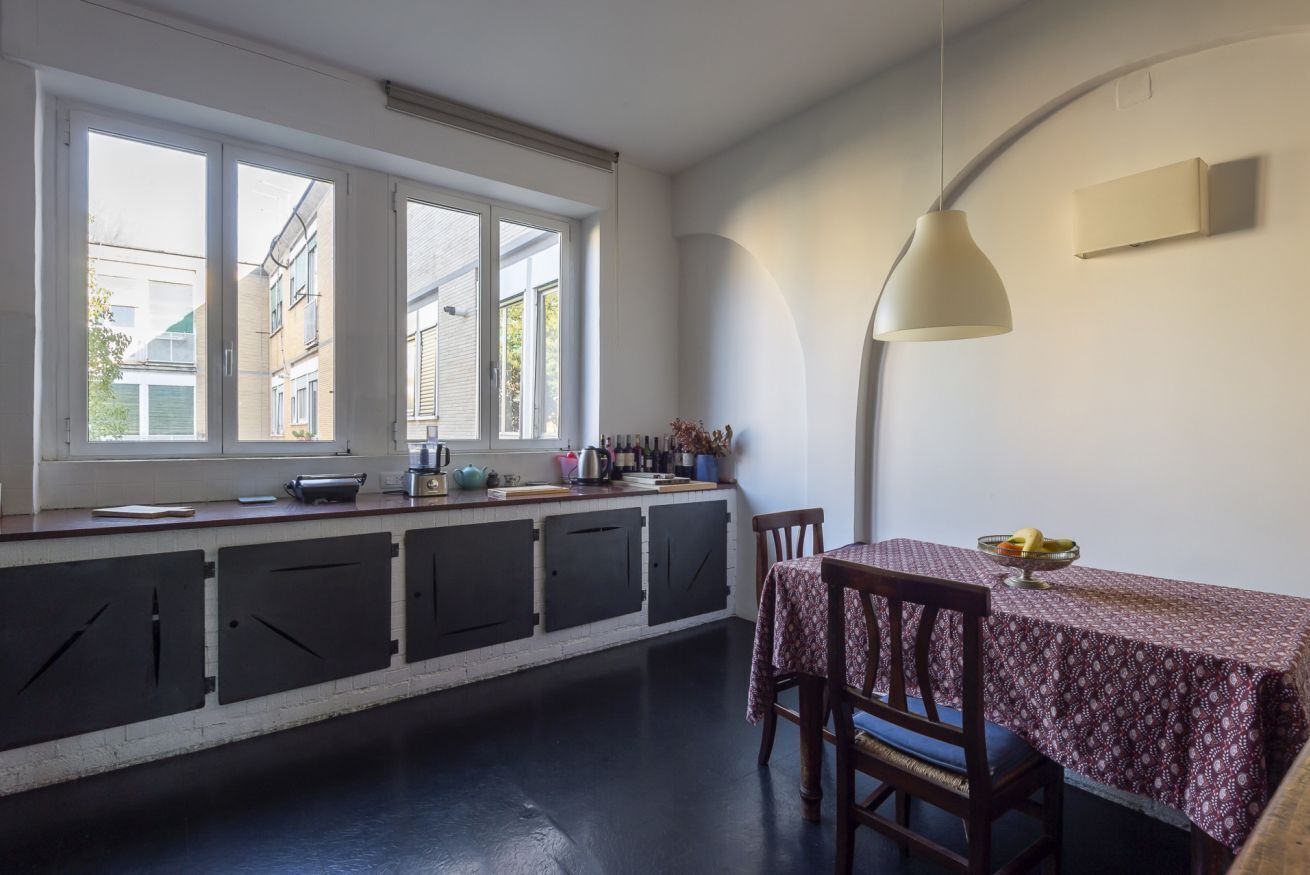 Een keuken met een groot raam, een eettafel met stoelen en een hanglamp.
