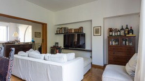 A living room with a white sofa, a television, a bookshelf, and a wooden cabinet with bottles. - Auditorium Enchanting Apartment (Roma)