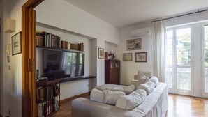 A living room with a sofa, a television, bookshelves, and a sliding glass door to the outside. - Auditorium Enchanting Apartment (Roma)