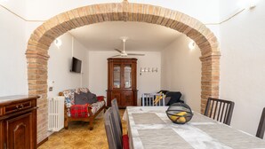 A dining area with a brick arch, a ceiling fan, a wooden cabinet, a radiator, a sofa, and a dining table with chairs. - Casa Roda – Your Home by Lake Trasimeno, Between Umbria and Tuscany (Castiglione del Lago)