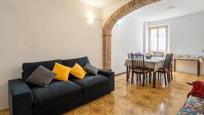 A room with a black sofa, a dining table with chairs, a brick archway, and a ceiling fan. - Casa Roda – Your Home by Lake Trasimeno, Between Umbria and Tuscany (Castiglione del Lago)