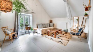 Ein gemütliches Wohnzimmer im Loft-Stil mit hohen Decken, einem Holztisch, einer Couch und zwei Sesseln.