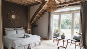 Ein Schlafzimmer mit einem großen Bett, einer Holztreppe, einem runden Tisch mit Stühlen und Blick ins Freie durch ein großes Fenster.