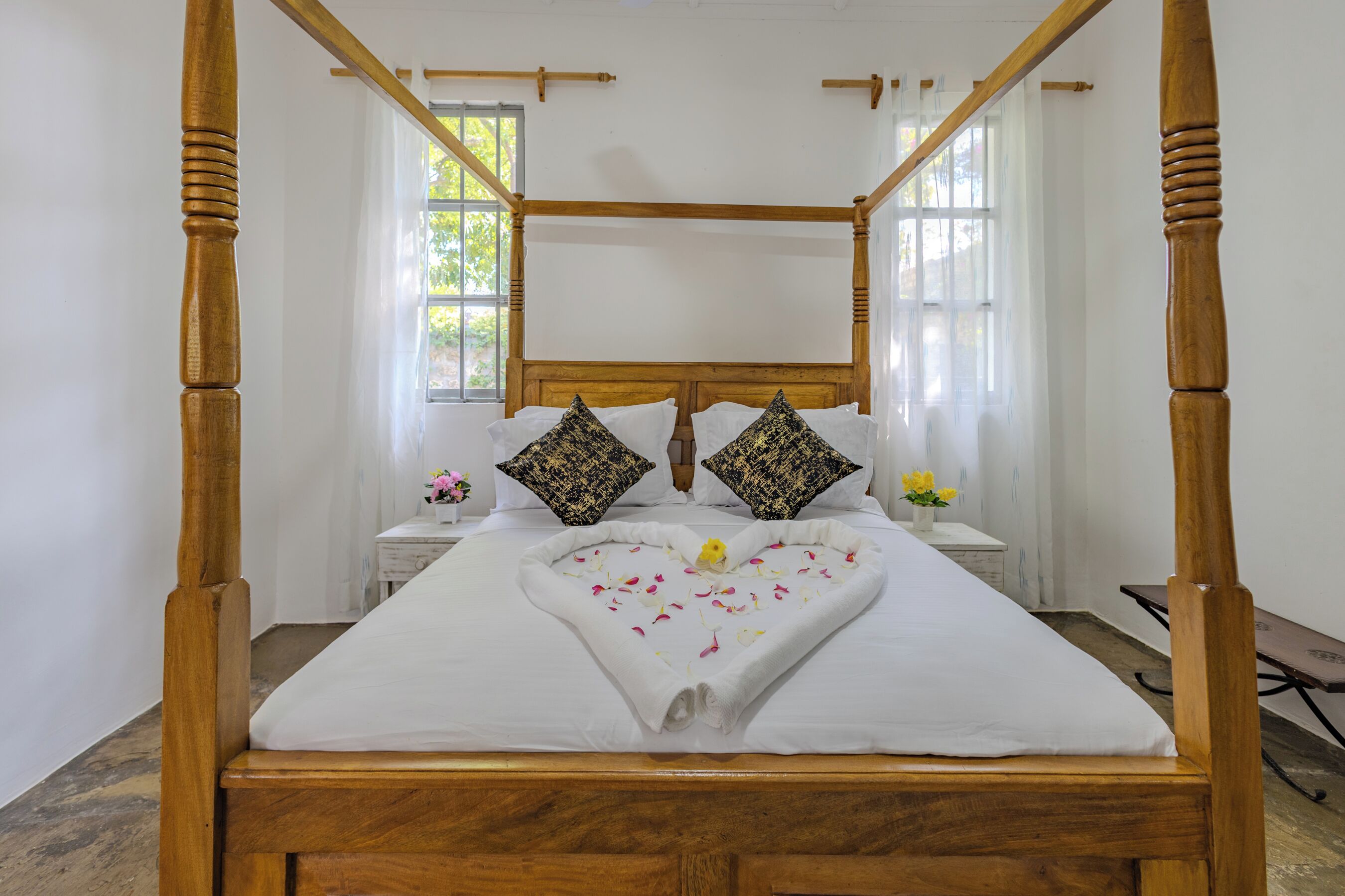 Una cama con dosel adornada con un arreglo de toallas y flores con forma de corazón sobre el edredón.