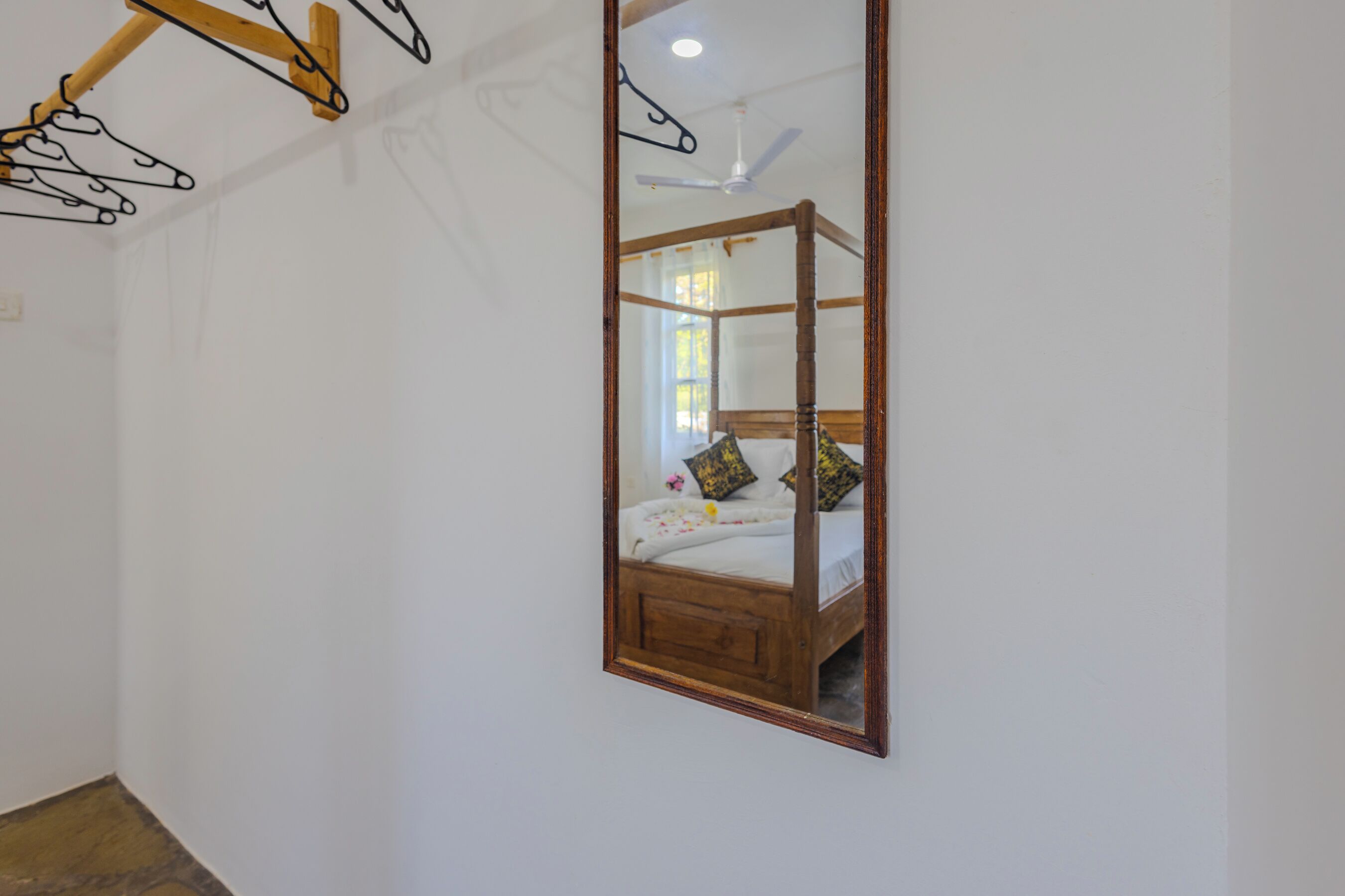 Un dormitorio con estructura de cama de madera, ventilador de techo y espejo en la pared.