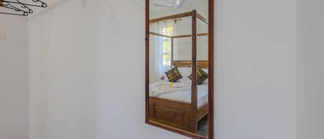 Un dormitorio con estructura de cama de madera, ventilador de techo y espejo en la pared.