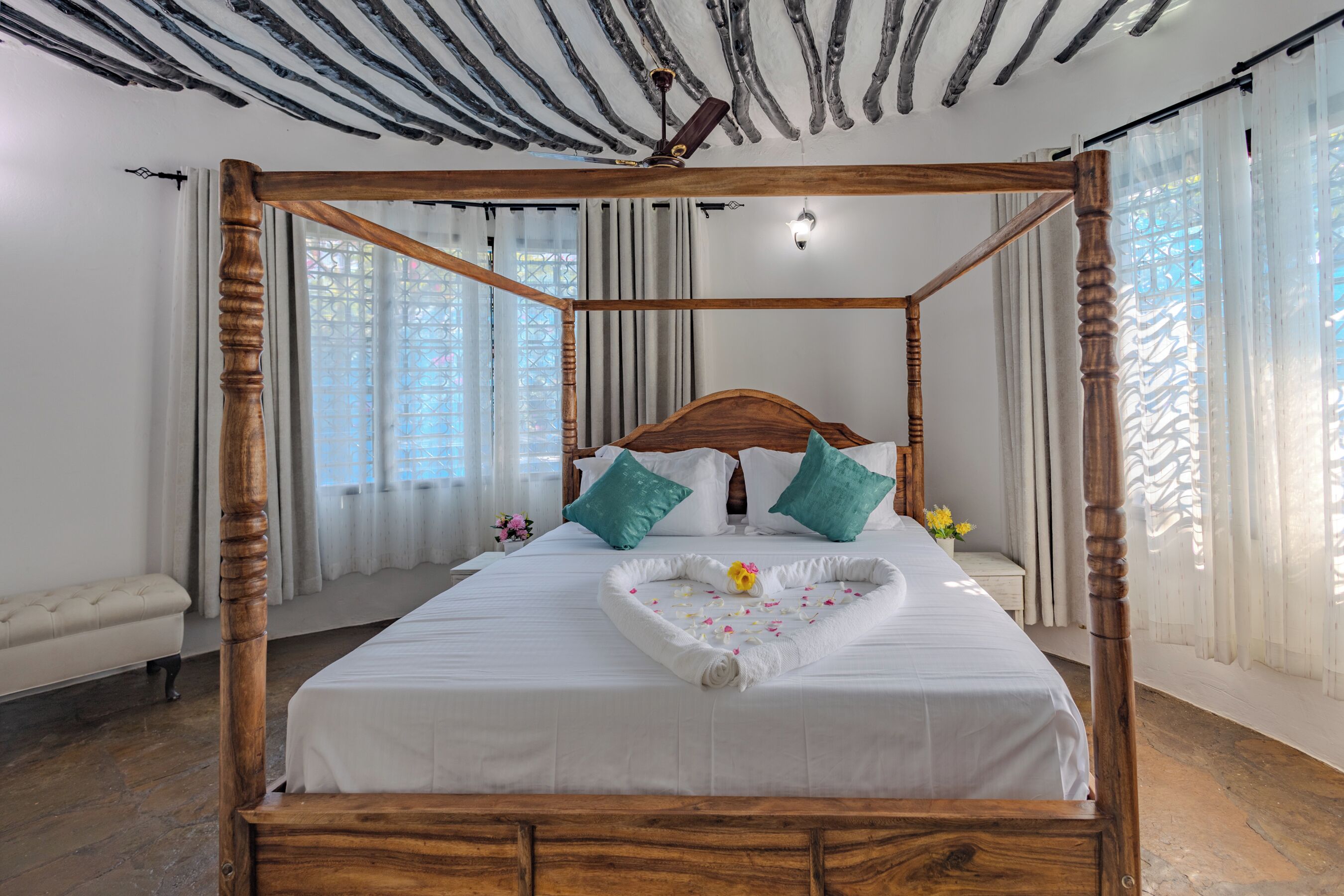 Uma cama de dossel com colcha em formato de coração, roupa de cama branca e almofadas verde-água.