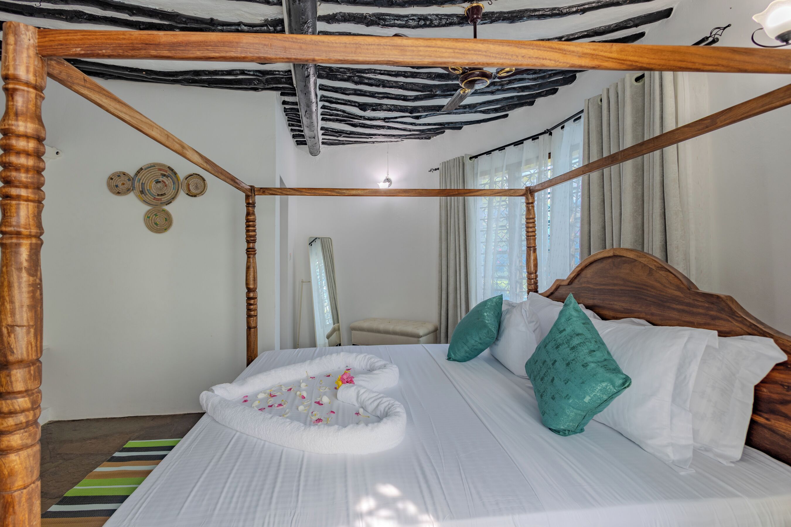 Een hemelbed met een witte baldakijn, een houten hoofdeinde en een decoratieve wanddecoratie.