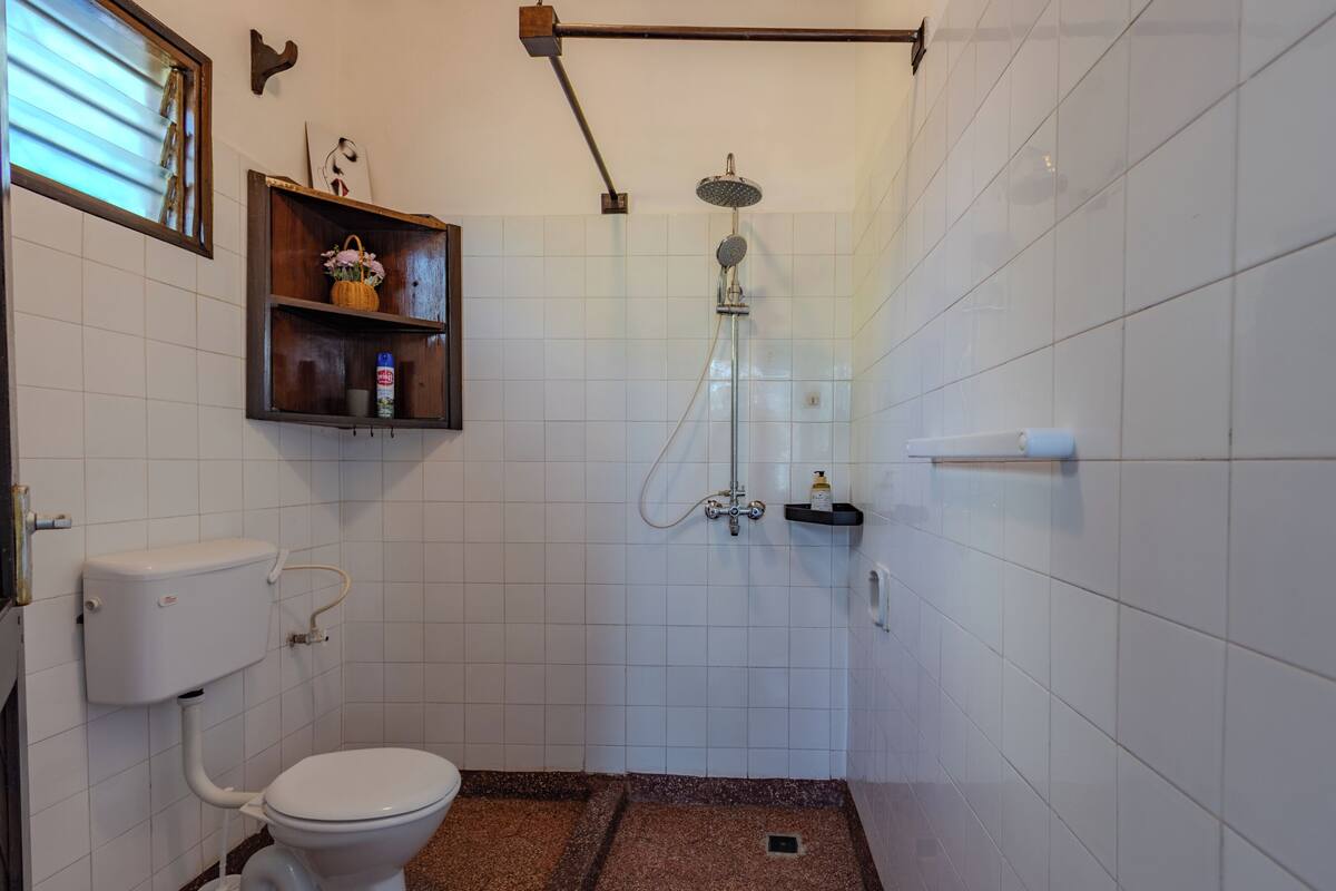 Un baño pequeño y limpio con inodoro, ducha y un estante con artículos de aseo.
