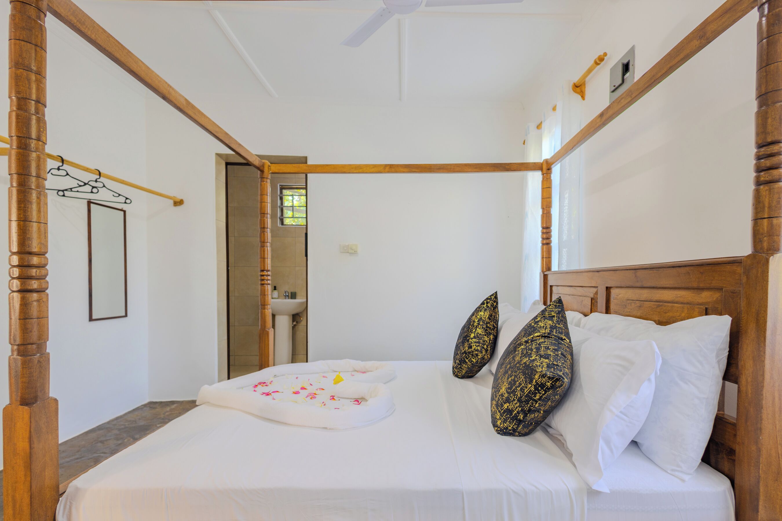 Una cama con dosel, ropa de cama blanca, almohadones decorativos, un cabecero de madera y una pequeña ventana al fondo.