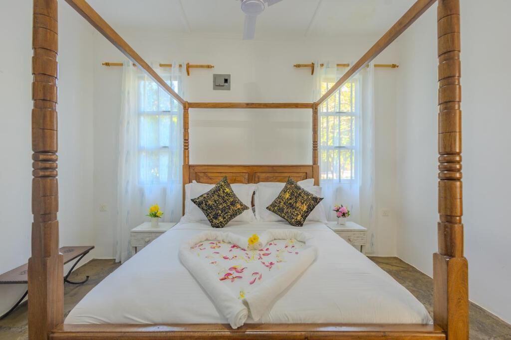 Una cama con dosel adornada con un arreglo floral en forma de corazón, dos almohadones decorativos y una mesita de noche con un florero.