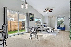 A spacious living room with a glass door leading to a backyard, a ceiling fan, and a large window. - South Austin Retreat: Pet-Friendly Townhouse (Austin)