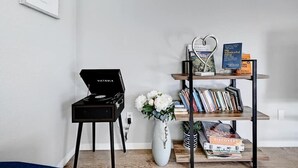 A room with a black speaker on a stand, a white vase with flowers, a bookshelf with books and a decorative item, and a framed map on the wall. - South Austin Retreat: Pet-Friendly Townhouse (Austin)