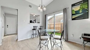 A dining area with a glass table and metal chairs, a kitchen area with a white countertop and a hanging light fixture, and a large window with curtains. - South Austin Retreat: Pet-Friendly Townhouse (Austin)