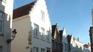 Una calle con edificios históricos, incluyendo un edificio blanco con techo a dos aguas y un farol negro.