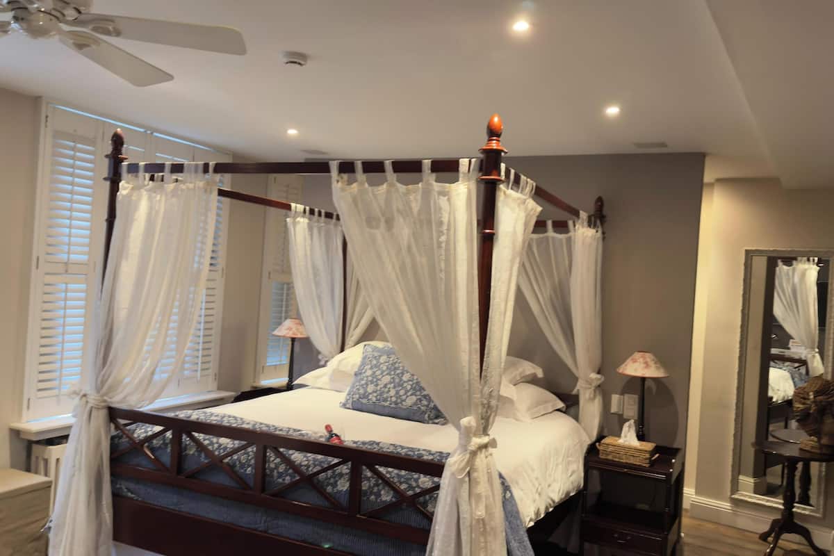 Een hemelbed met wit beddengoed, een houten hoofdbord en een nachtkastje met een lamp.