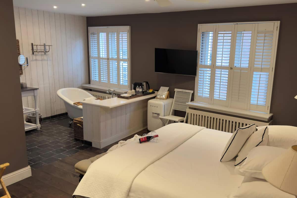 Een moderne hotelkamer met een groot bed, een zithoek met een stoel en een klein tafeltje, een badkamer met een bad en een toilet, en een aan de muur bevestigde televisie.