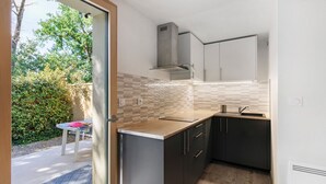 Une cuisine compacte dotée d’une cuisinière intégrée, un petit coin repas avec une table et des chaises, et une vue sur la verdure à l’extérieur.