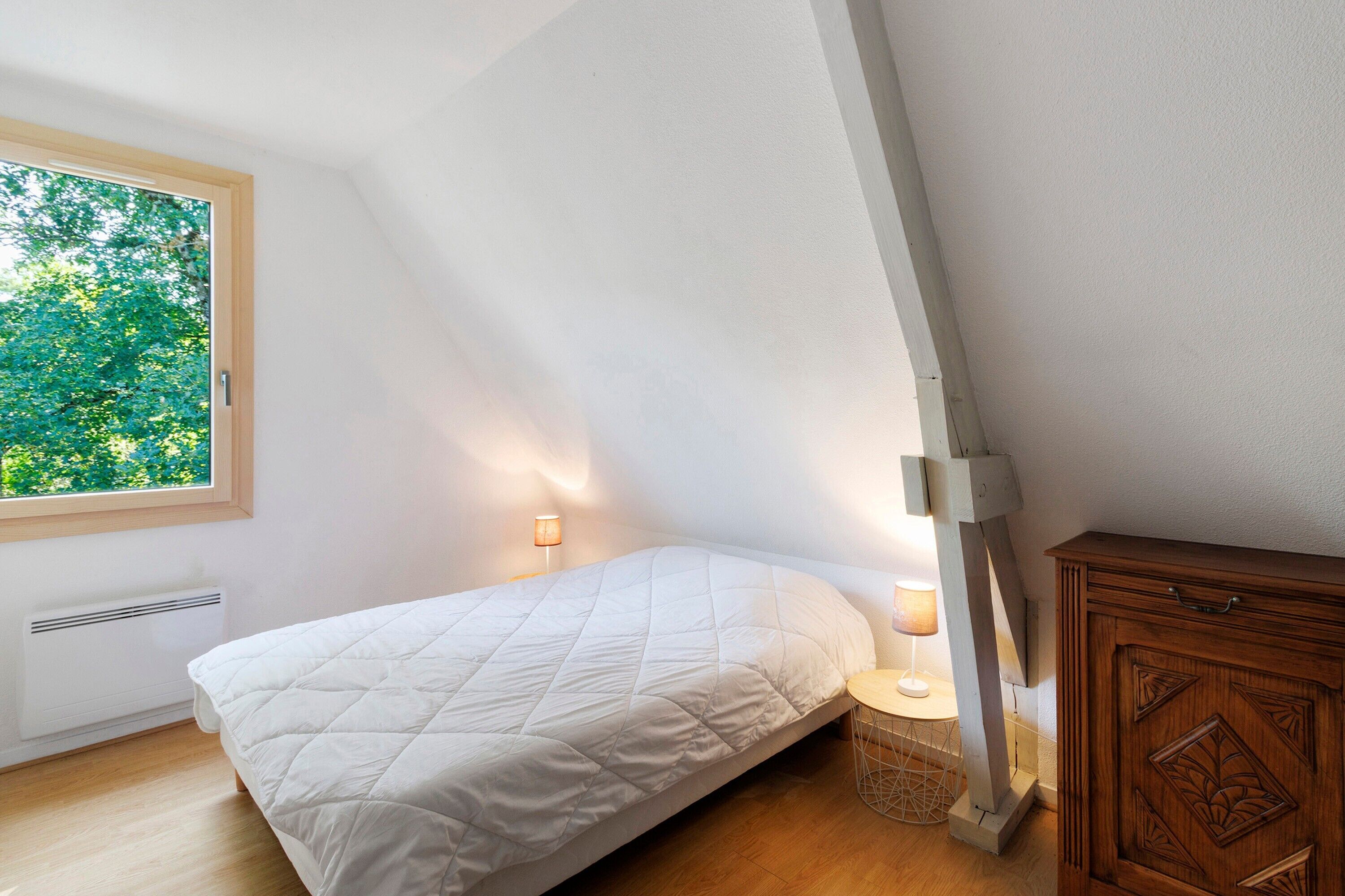 Una camera da letto con un letto, una finestra, una lampada da comodino, un armadietto in legno e un termosifone.