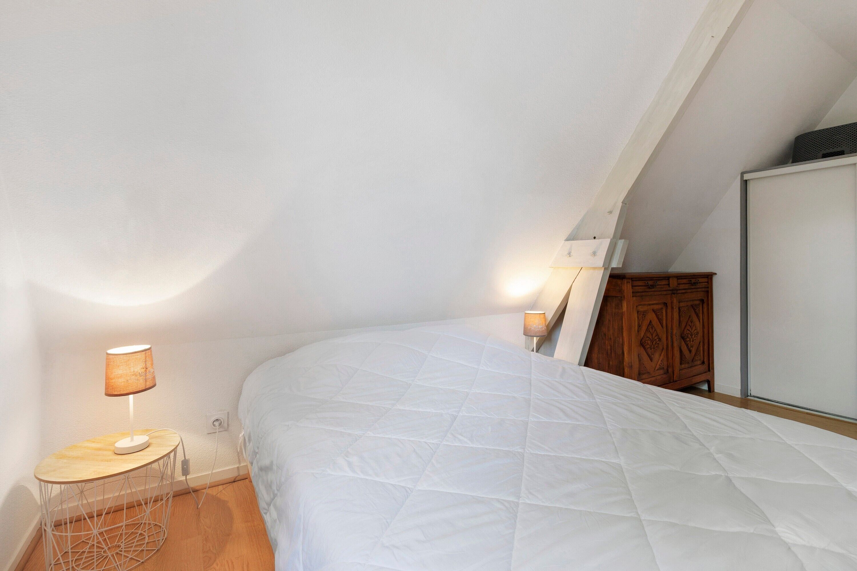 A bedroom with a bed, a small round table with a lamp, and a wooden cabinet.