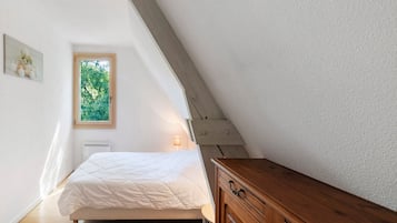 Une chambre à coucher avec un lit, une commode en bois, une fenêtre donnant sur un paysage verdoyant et une lampe fixée au mur.
