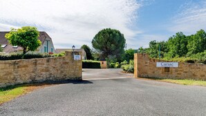 Une entrée fermée par un portail mène à une propriété appelée « Carsac », qui est entourée de murs en pierre et s’ouvre sur un ciel dégagé.