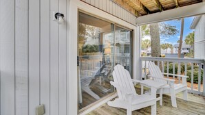 Eine überdachte Veranda mit weißen Adirondack-Stühlen, einer Glastür und Blick auf die Nachbarschaft.