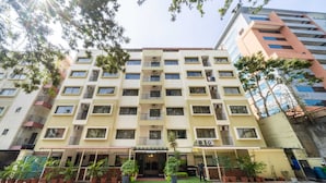 A multi-story hotel with a central entrance, balconies, and potted plants around the entrance. - Midtown Suites  Marathahalli (Bengaluru)